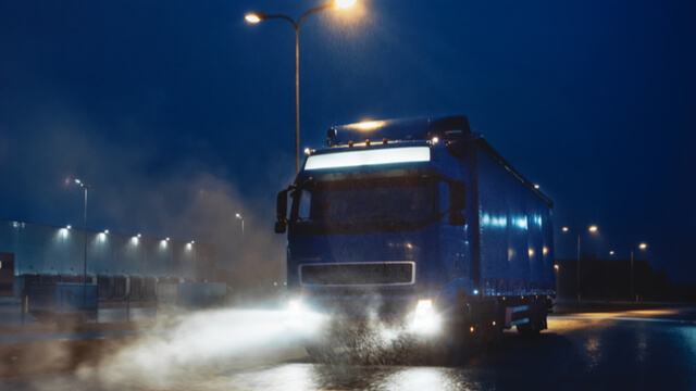 Foto de um caminhão de noite com os farois acesos.